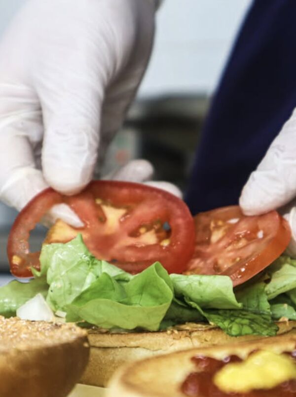 Préparation d'un burger : tomate et salade posées à la main